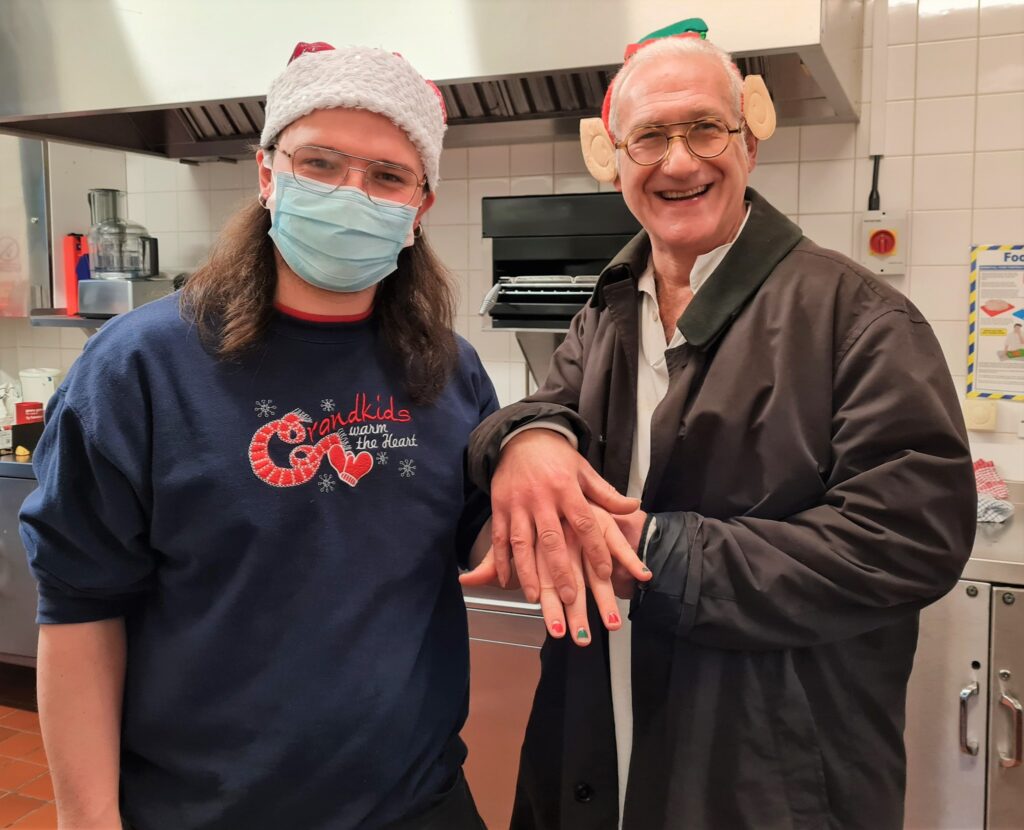 Two volunteers standing in the kitchen, one showing off red and green nail polish
