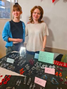 Two women standing behind a table displaying colourful plastic jewellery